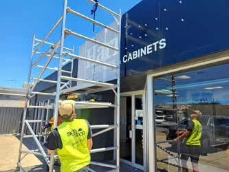 Workers moving a scaffold to continue work on building signage, outside on a sunny day