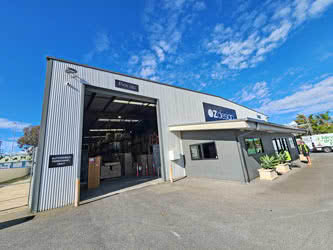 Front-left outside view of large warehouse building with open roller door, sunny day