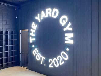 Large LED sign, lit up, mounted on the wall inside a building, belonging to 'The Yard Gym'