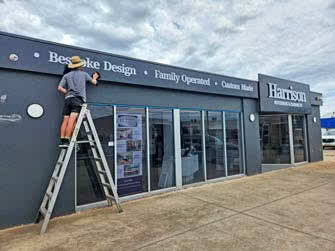 Worker on ladder putting finishing touches on building signage of a business, outside on an overcast day