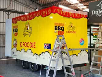 Rear side view of an enclosed food and drink trailer inside a workshop, belonging to K Foodie Korean Food