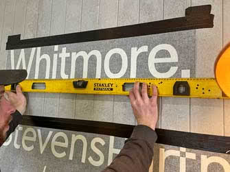 Closeup of worker installing letter signage onto an indoors office wall