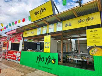 A food stall with menus and signage, belonging to Xeo Xeo sizzling pancakes, outside on an overcast day